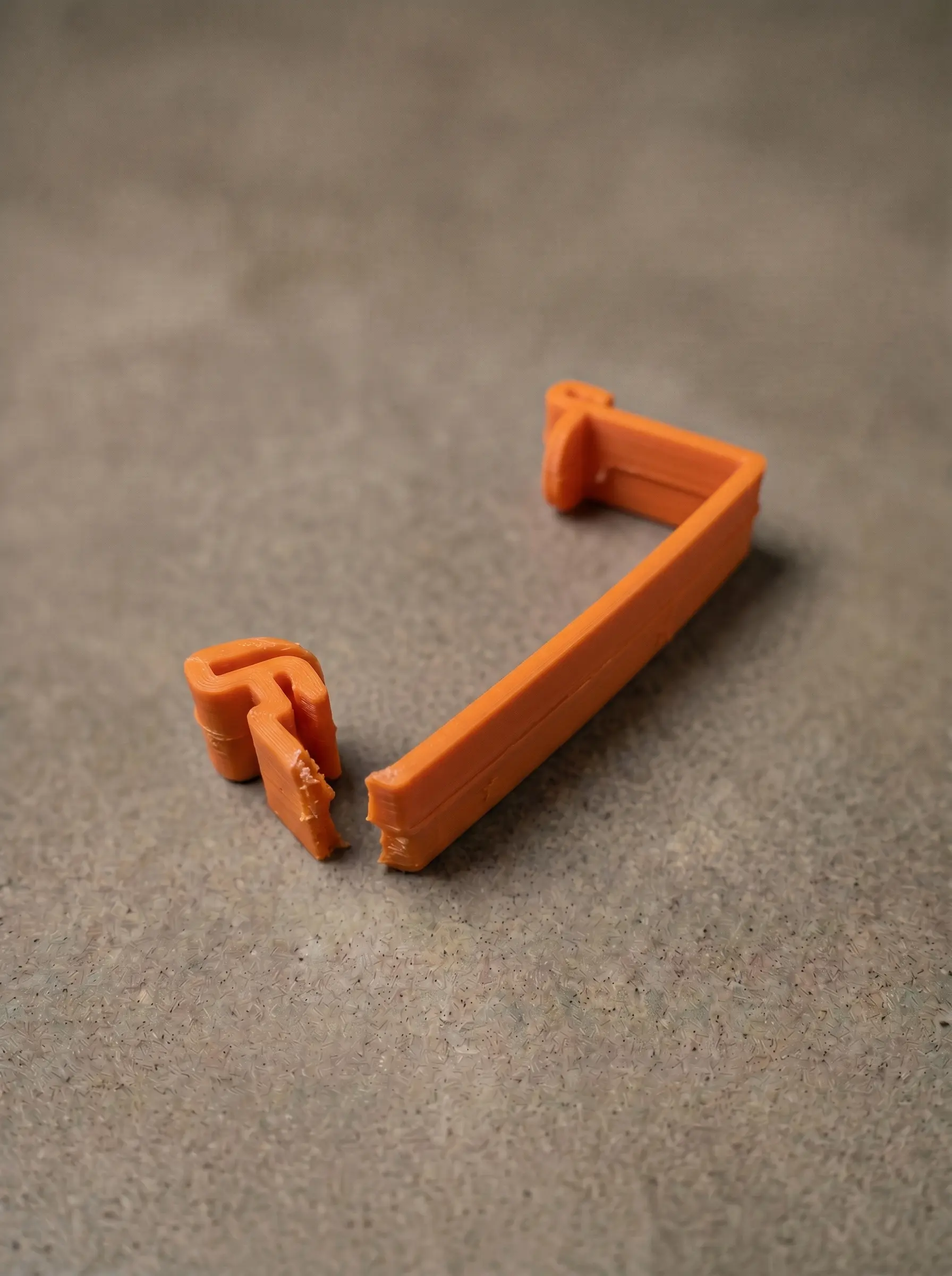 Broken original transport-line bracket — orange moulded plastic, snapped through the corner